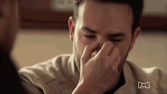 a man is covering his nose with his hand while sitting at a table .