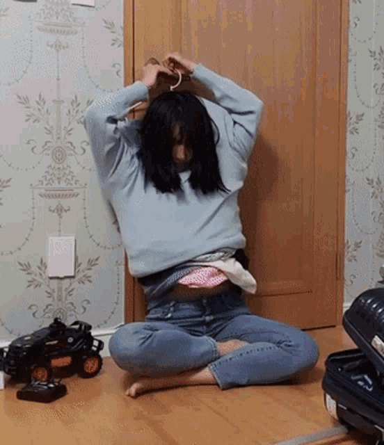 a woman in a blue sweater sits on the floor next to a toy car