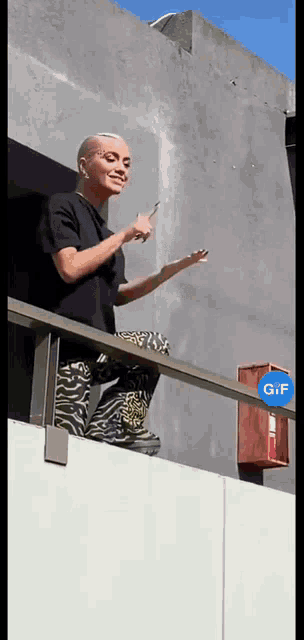 a woman is standing on a balcony with a gif sign in the background