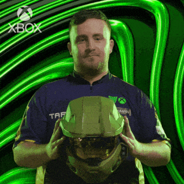 a man in an xbox shirt holds a helmet in front of a green background