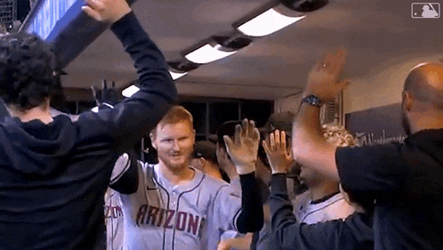 a group of baseball players are giving each other a high five in a locker room .