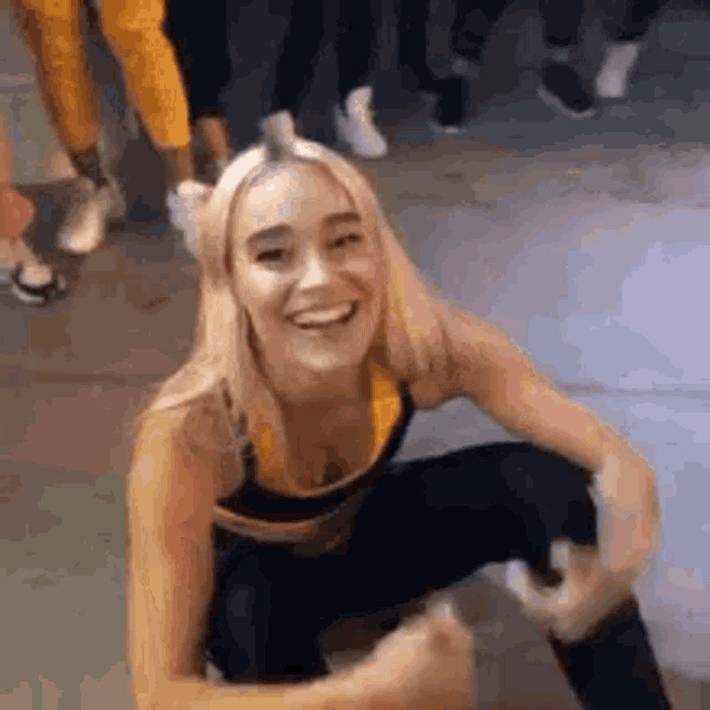 a woman is squatting down and smiling while a group of people are standing behind her .