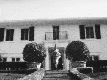 a black and white photo of a man standing in front of a large house .