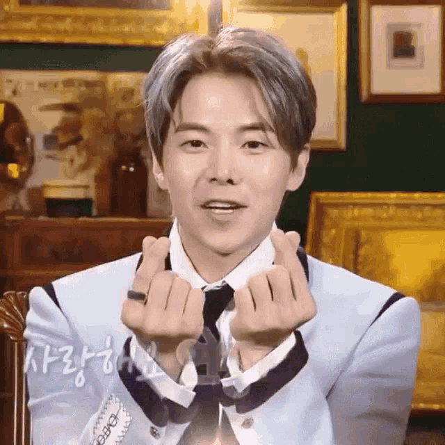 a young man in a suit and tie is making a heart with his hands .