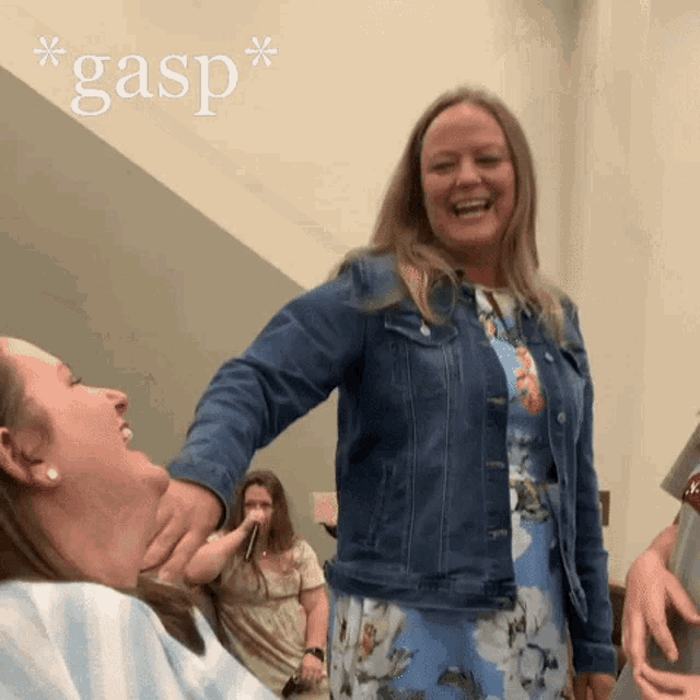a woman in a denim jacket is holding another woman 's neck and laughing
