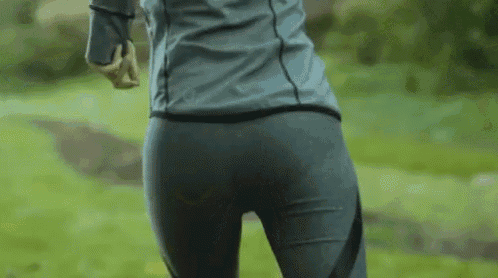 a woman in leggings and a jacket is running in a park