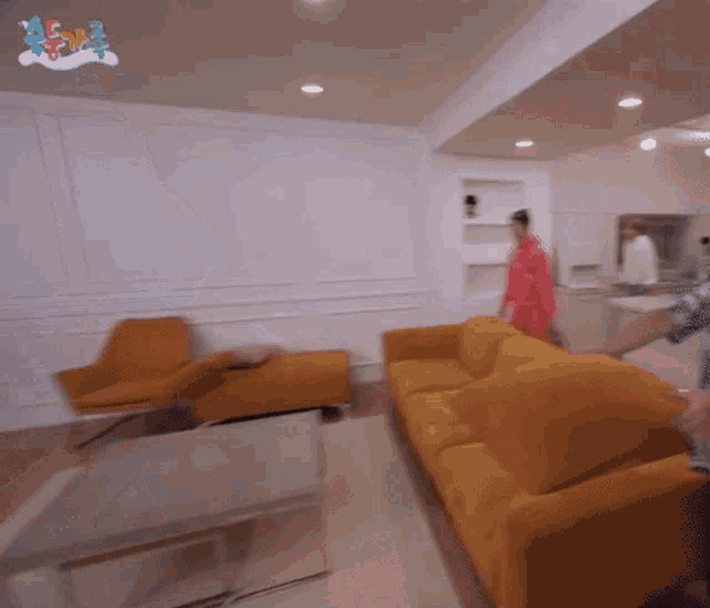 a man in a red shirt is standing in a living room with a yellow couch