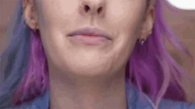a close up of a woman 's face with purple hair and earrings
