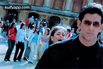 a man wearing sunglasses is standing in front of a crowd of people dancing .
