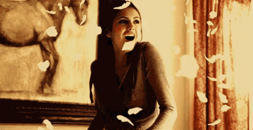 a woman is laughing while feathers are flying around her .