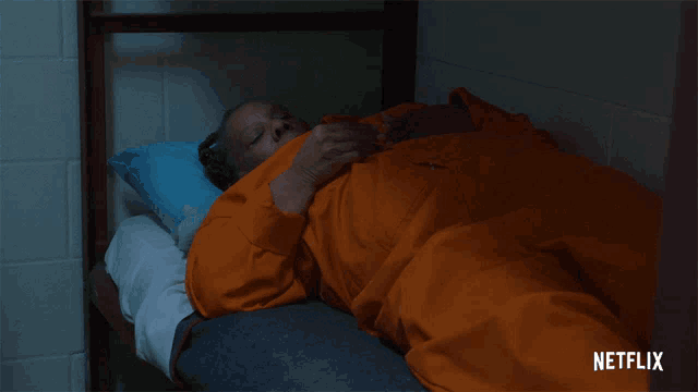 a man in an orange prison uniform is laying on a bed with a netflix logo in the corner