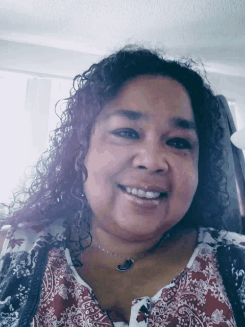 a woman with curly hair is smiling and wearing a paisley top