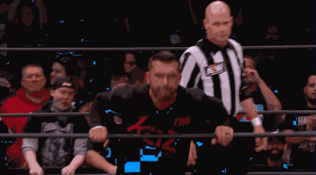 a man in a wrestling ring with a shirt that says ' aew ' on it stands next to a referee