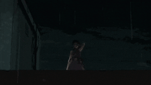 a woman in a purple dress is standing in the dark with her hands on her head .