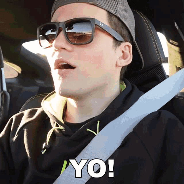 a man wearing sunglasses and a hat is sitting in a car with the word yo written in white