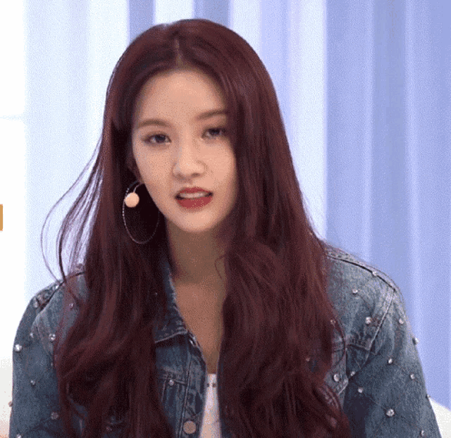 a woman with red hair is wearing a denim jacket and hoop earrings