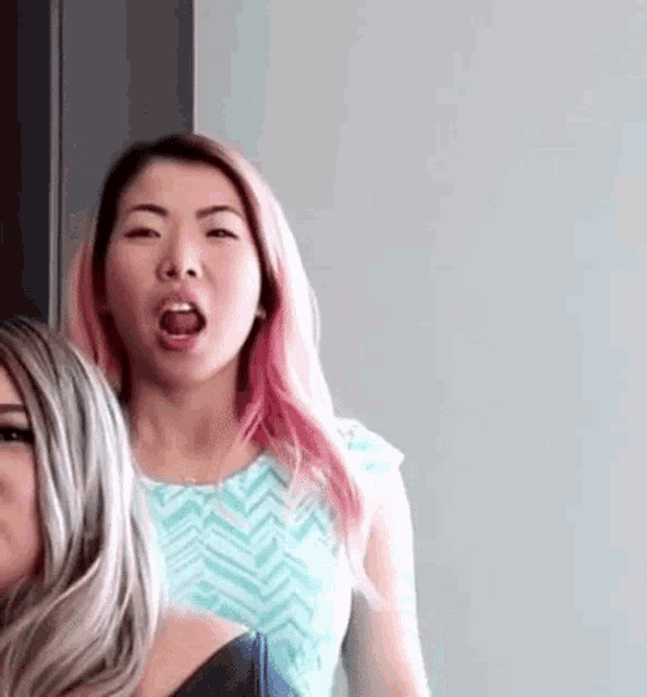 a woman with pink hair is making a funny face while standing next to another woman with blonde hair .