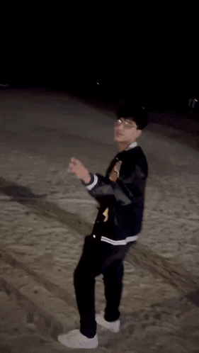 a man wearing glasses and a black jacket is pointing at the camera at night .