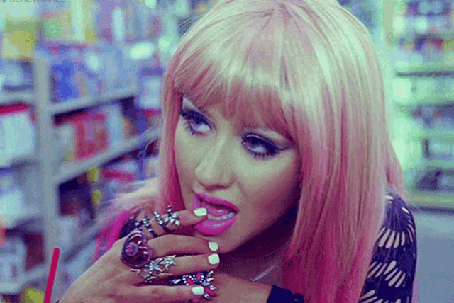 a woman with pink hair and rings on her fingers is eating something