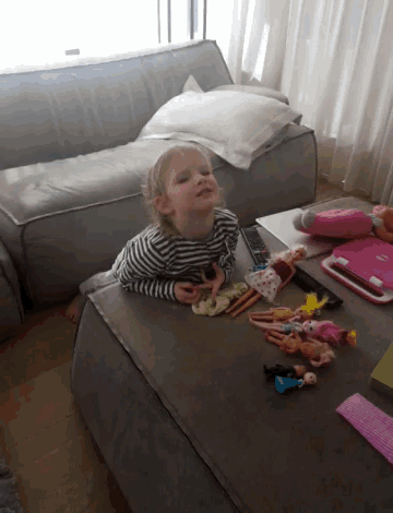 a little girl sits on a couch playing with dolls
