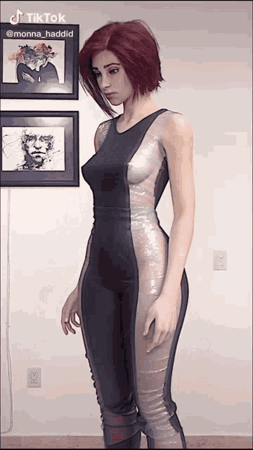 a woman in a black and silver jumpsuit is standing in front of a wall with three framed pictures on it and a tiktok sticker