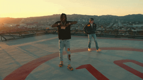 two men are standing on a rooftop with a circle in the middle that has the letter t on it