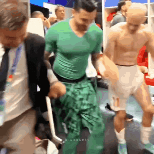 a man in a green shirt is standing in a locker room with other people
