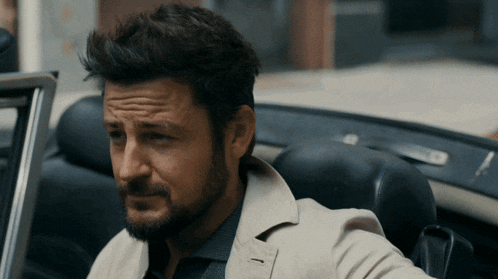 a man with a beard is sitting in the back seat of a convertible car