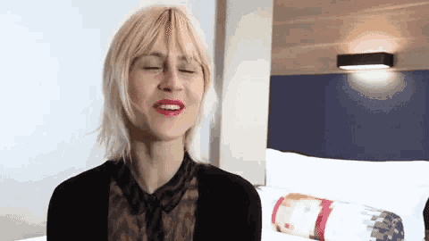 a woman with blonde hair and red lipstick is sitting on a bed with her eyes closed