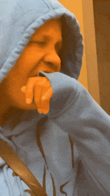 a person wearing a blue hoodie has their hand on their mouth