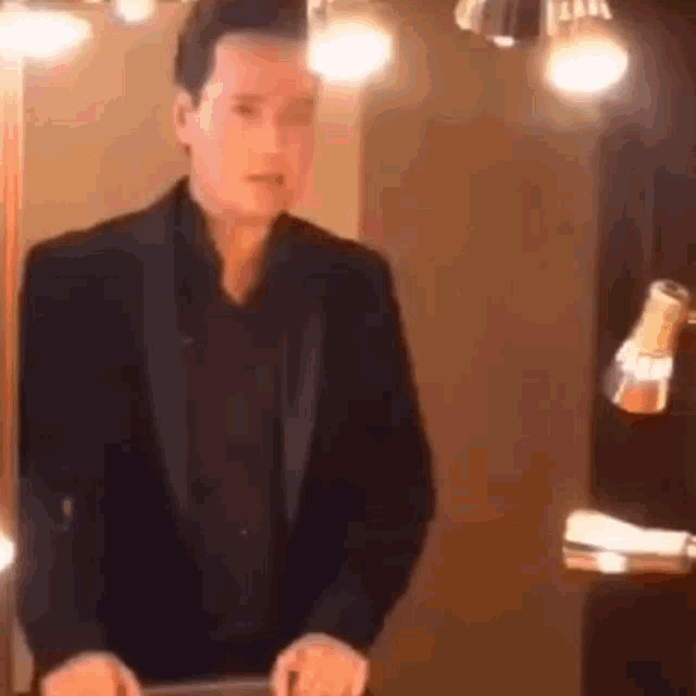 a man in a suit and black shirt is standing in front of a mirror .