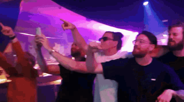a group of men are dancing in a dark room with purple lights behind them