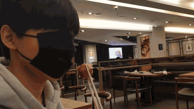 a man wearing a black face mask sits in a restaurant