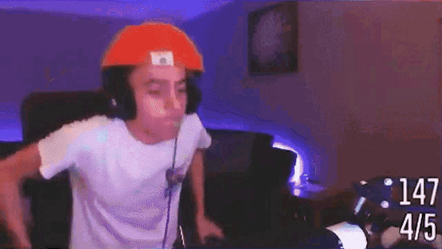 a man wearing headphones and an orange hat is dancing in front of a screen that says 147 4/5 on it
