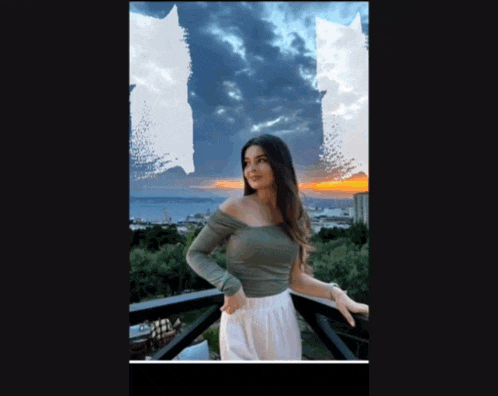 a woman in a green off the shoulder top stands on a balcony with a sunset in the background