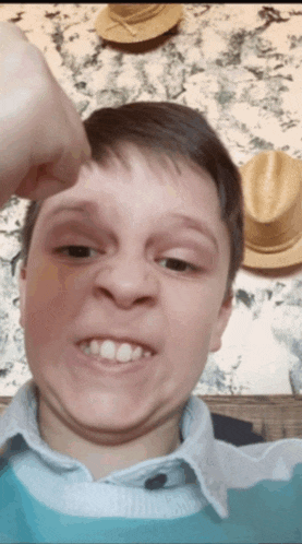 a young boy making a funny face with his hand on his forehead in front of straw hats