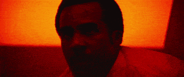 a close up of a man 's face with a red light behind him .