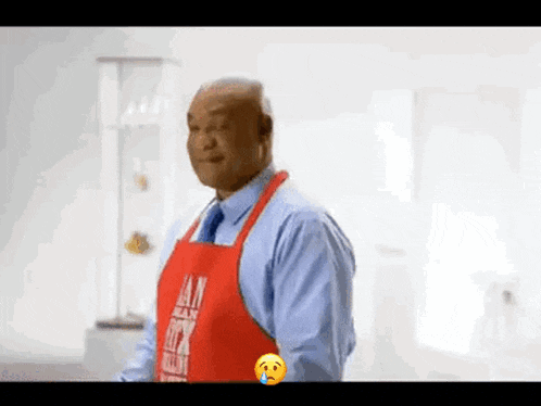 a man wearing a red apron and a blue shirt is standing in a kitchen .