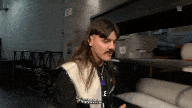 a man with long hair and a mustache is standing in a room next to a sign that says exit