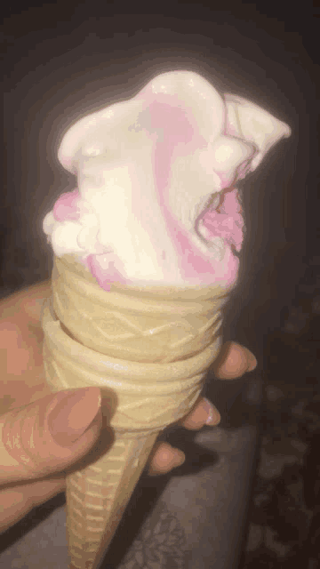 a person holding a pink and white ice cream cone with a bite taken out of it