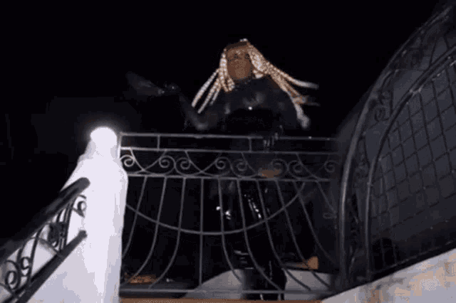 a woman with blonde braids is standing on a railing at night .