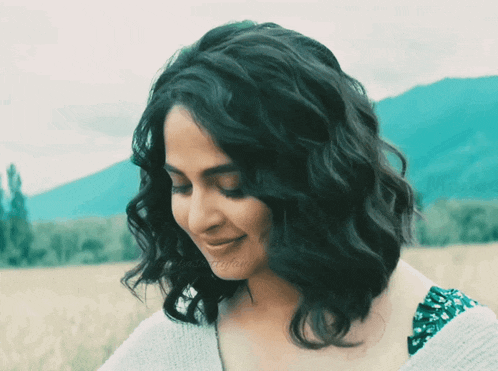 a woman with curly hair is smiling in a field with mountains in the background and a hashtag that starts with the letter a