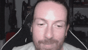 a man with long hair and a beard is sitting in a chair looking at the camera .