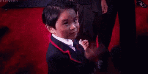 a little boy in a tuxedo is standing on a red carpet .