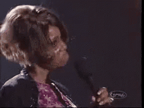 a woman is singing into a microphone with the word whaat written on the bottom