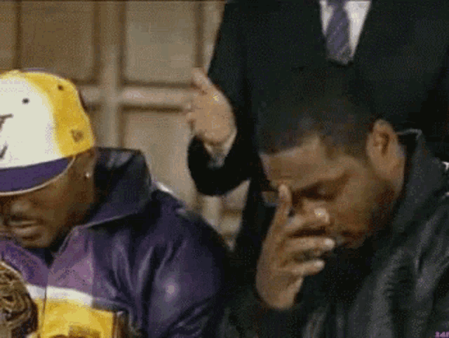 two men are sitting next to each other and one of them is wearing a hat with the letter t on it