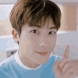 a close up of a young man wearing a blue sweater pointing up with his finger .
