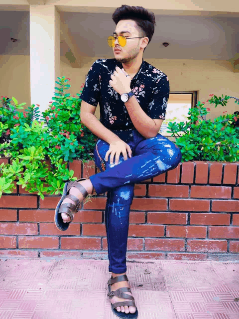 a young man is sitting on a brick wall wearing sunglasses and a watch