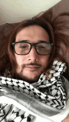 a man wearing glasses and a scarf is laying on a couch