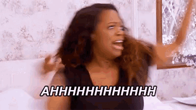 a woman is sitting on a bed with her hands in the air and screaming .